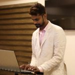 Young professional in a white suit using a laptop indoors, focused on work in Ahmedabad, India.